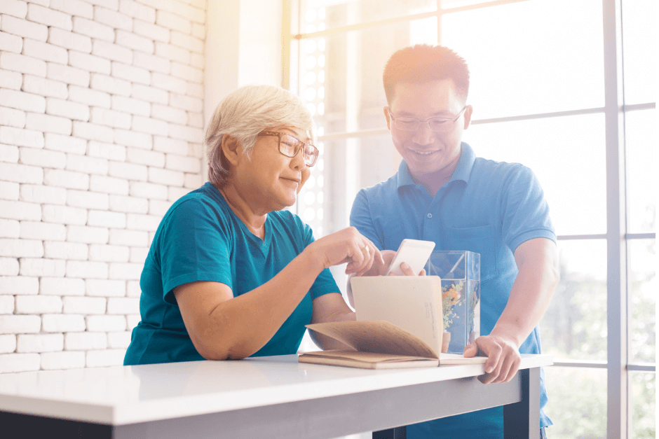 A younger masculine-presenting individual showing an older feminine-presenting individuals how to use their phone.