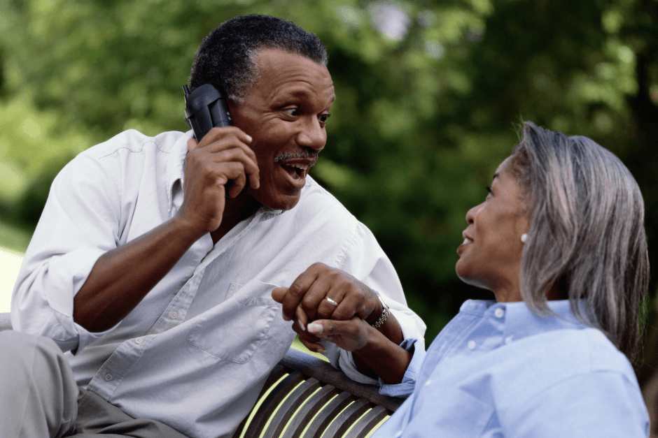 A couple smiling at each other as the masculine-presenting individual is using his phone.