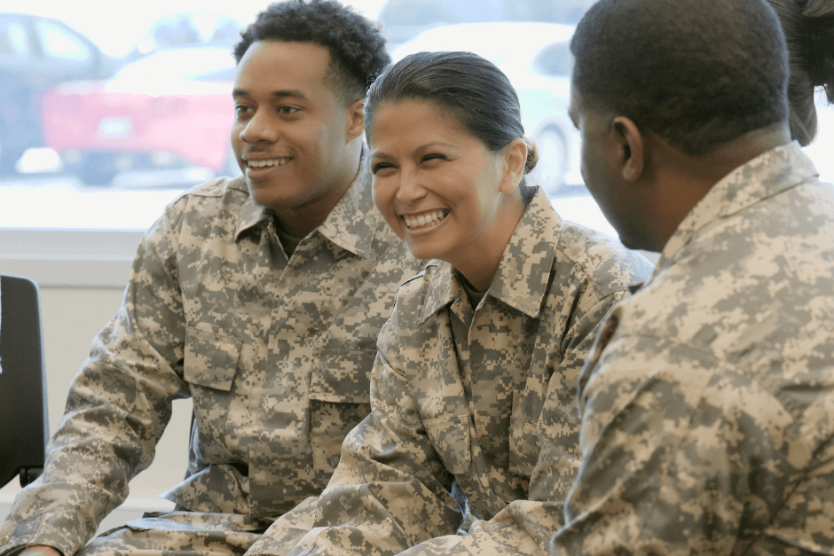 Three smiling individuals sitting and smiling in camouflage attire.